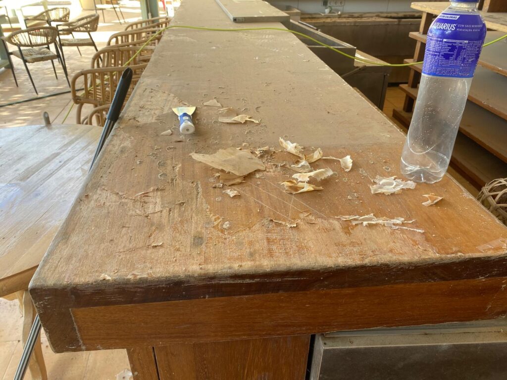 Iroko bar top before restoration with flaking paint and varnish