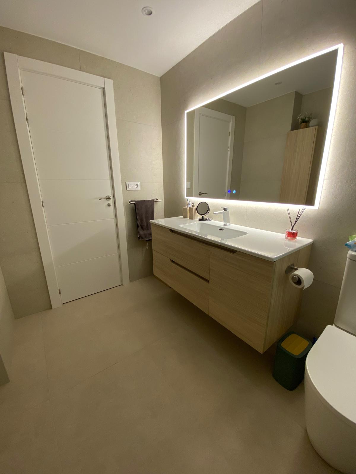 Renovated bathroom in Gata de Gorgos with wooden vanity and backlit mirror by Mayra Studio