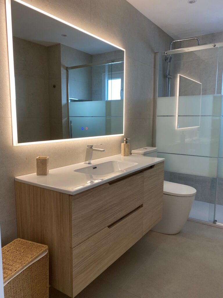 Wooden vanity and backlit mirror in a renovated bathroom